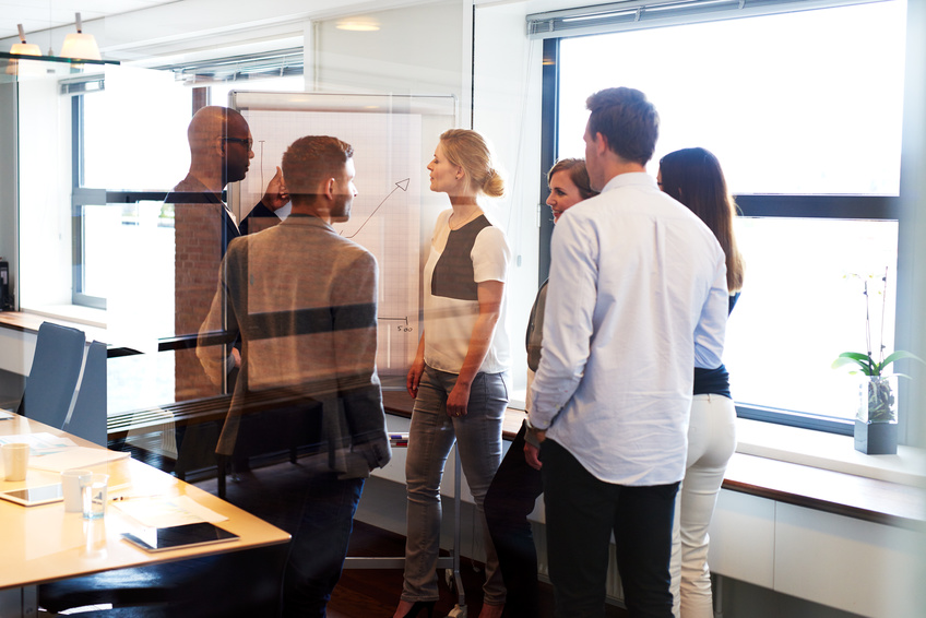Group of executives standing in conference room gathered around white board