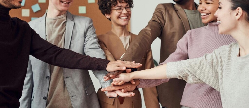 A diverse group of people holding hands in a circle in an office setting, symbolizing unity and teamwork.